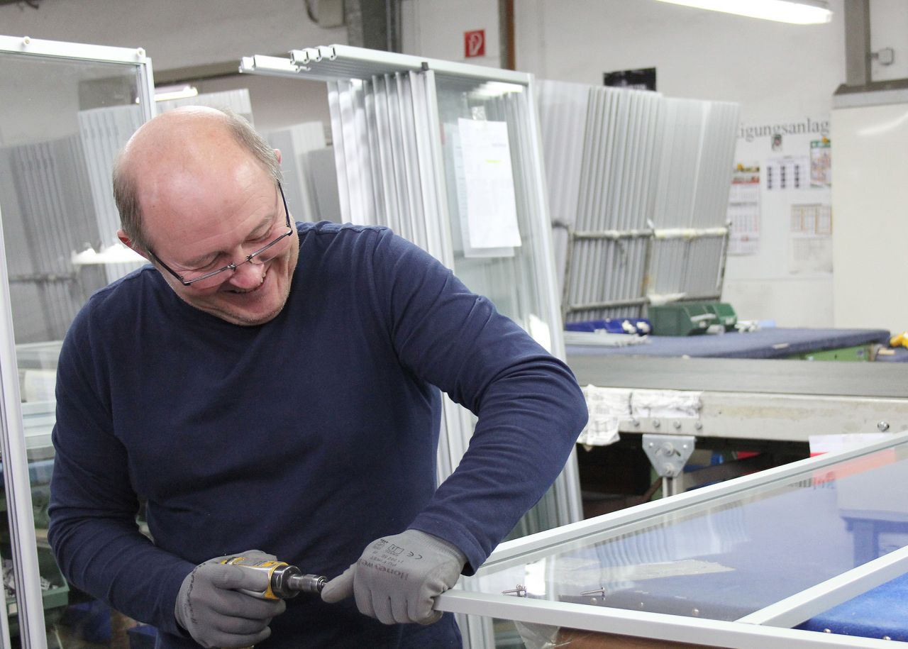 Schulung Produktion Imagebild Produktionsmitatbeiter mit Werkzeug an einer Duschkabinenwand